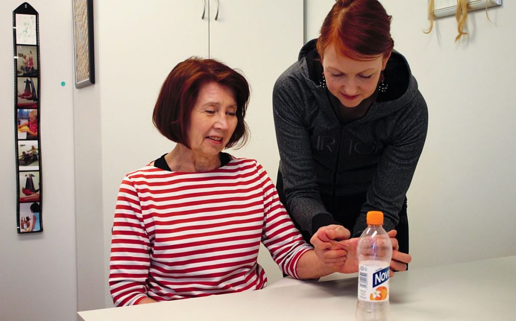 Terapianurkan toimintaterapeutin palvelut aikuisille, kuvassa terapeutti auttamassa naista tarttumaan vesipulloon